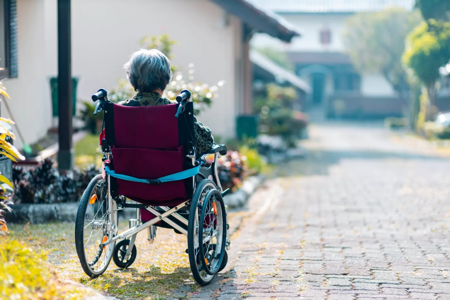 A middle-aged woman in a wheelchair facing away from the camera, outdoors in a driveway